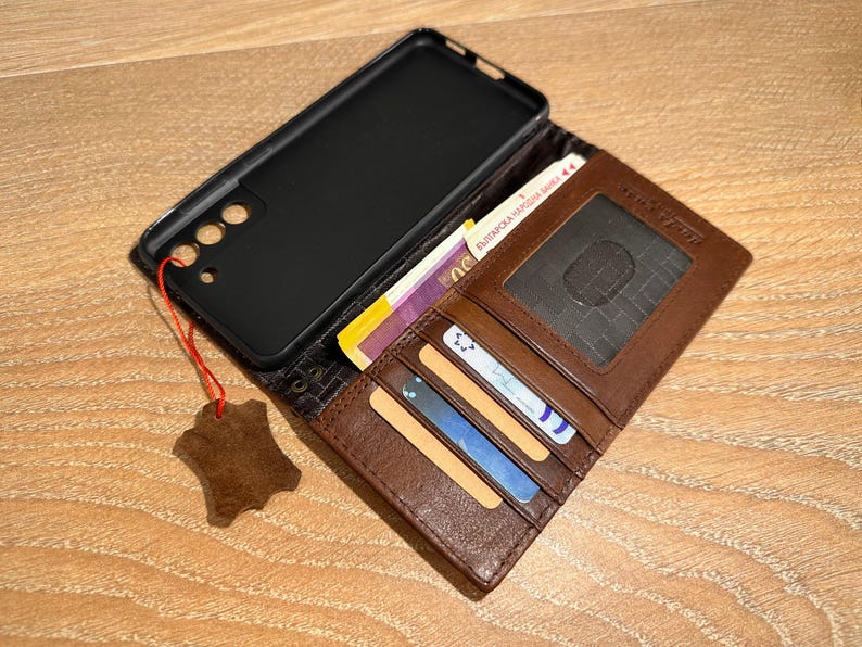 A brown wallet with a black case and various cards is placed on a wooden surface.