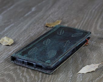 May include: A dark blue leather phone case with a leaf pattern. The case is lying on a wooden surface.