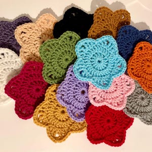 Pode incluir: Uma coleção de apliques em forma de estrela de crochê feitos à mão em várias cores, incluindo branco, vermelho, roxo, verde, azul e laranja. Estes elementos decorativos são ideais para projetos de artesanato e embelezamentos.