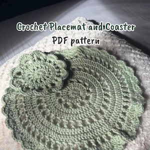 May include: A sage green crochet placemat and matching coaster set featuring a circular design with openwork stitches and a scalloped edge. The text "Crochet Placemat and Coaster PDF pattern" is displayed in white lettering over the items.