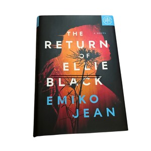 K&ouml;nnte beinhalten: Ein Buchcover mit einem dunklen Hintergrund und einer Silhouette einer Person mit einer Blume davor. Der Titel lautet "The Return of Ellie Black" von Emiko Jean.