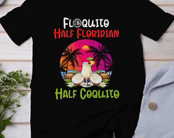 Könnte beinhalten: Schwarzes T-Shirt mit einer weißen Grafik eines Sonnenuntergangs, Palmen und einem Kokosnussgetränk. Der Text "Floquito Half Floridian Half Coquito" ist auf das T-Shirt gedruckt.