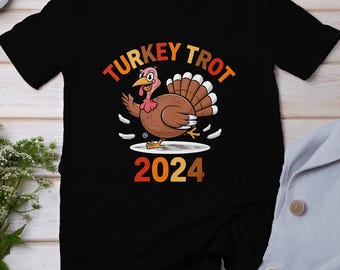 Könnte beinhalten: Schwarzes T-Shirt mit einem Cartoon-Truthahn, der auf einem Teller läuft. Der Text "TURKEY TROT 2024" ist auf dem Shirt aufgedruckt.