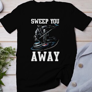 Könnte beinhalten: Schwarzes T-Shirt mit einer weißen Grafik eines Curlers, der einen Stein fegt. Der Text "Sweep You Away" ist unter dem Bild gedruckt.