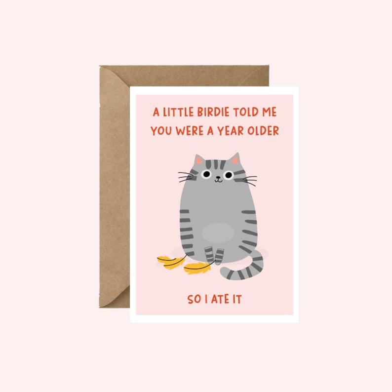 Puede incluir: Tarjeta de felicitaci&oacute;n con un gato de dibujos animados gris con rayas negras, sobre un fondo rosa. El texto dice: &laquo;A LITTLE BIRDIE TOLD ME YOU WERE A YEAR OLDER SO I ATE IT&raquo;. La tarjeta est&aacute; dentro de un sobre marr&oacute;n.
