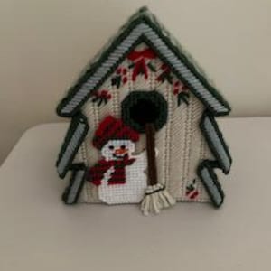May include: A handmade, needlepoint birdhouse in the shape of a Christmas tree. The birdhouse features a snowman with a red hat and scarf, a broom, and festive red and green accents. The roof and trim are green.