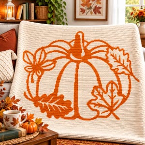 May include: A cream-colored crochet blanket featuring a large, centered orange pumpkin graphic surrounded by various autumn leaf designs. The textile has a consistent, textured stitch pattern throughout, showcasing a clear, bold contrast between the orange and cream yarn colors.