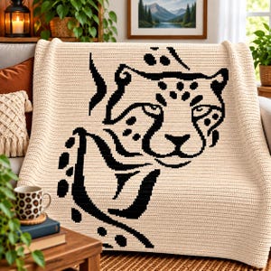 May include: A cream-colored crocheted throw blanket featuring a large, bold black graphic design of a cheetah's face and upper body. The knit texture is uniform throughout the fabric, showcasing a clear, high-contrast feline illustration.