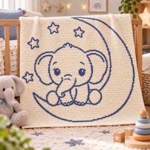 May include: A cream-colored crochet blanket featuring a dark blue graphic design of a baby elephant sitting on a crescent moon surrounded by four stars. The blanket has a textured knit pattern and is displayed draped over a wooden crib railing.