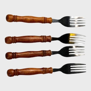 May include: Four forks with stainless steel tines and wooden handles. The handles are a warm brown color, with a rounded, bulbous design. The tines are silver and have a classic, curved shape. The forks are arranged horizontally against a light background.