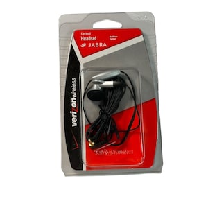 Puede incluir: Auriculares Jabra en un embalaje de plástico transparente. Los auriculares son negros y plateados, con un cable negro. El paquete tiene el logotipo de Verizon Wireless y el logotipo de Jabra. El paquete es rojo y gris.