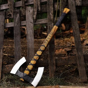 May include: A double-headed axe with a wooden handle wrapped in black leather. The handle is inscribed with the word "TYR" in runes. The axe is leaning against a wooden fence.
