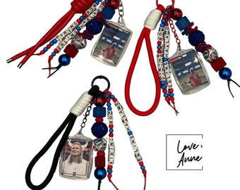 May include: Three keychains featuring Erling Haaland, each with a wrist strap, colourful beads, and lettered cubes spelling VIKING and ERLING HAALAND. Two keychains have red straps and one has a black strap, all attached to clear photo charms.