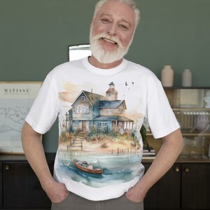 May include: A white t-shirt with a watercolor illustration of a house on a beach with a boat in the water. The house has a blue roof and white trim. The boat is red and white.