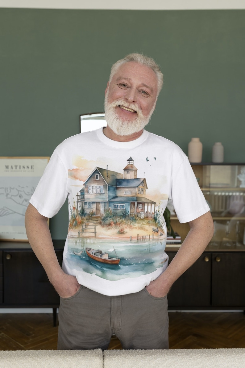 May include: A white t-shirt with a watercolor illustration of a house on a beach with a boat in the water. The house has a blue roof and white trim. The boat is red and white.