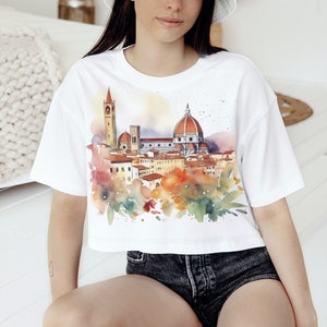 K&ouml;nnte beinhalten: Wei&szlig;es, bauchfreies T-Shirt mit einem Aquarell-Motiv der Skyline von Florenz, einschlie&szlig;lich des Doms und anderer Geb&auml;ude. Das Shirt hat eine lockere Passform und kurze &Auml;rmel.