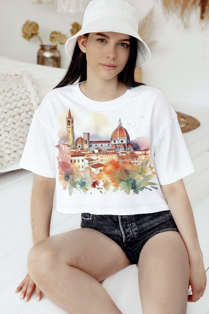 K&ouml;nnte beinhalten: Wei&szlig;es, bauchfreies T-Shirt mit einem Aquarell-Motiv der Skyline von Florenz, einschlie&szlig;lich des Doms und anderer Geb&auml;ude. Das Shirt hat eine lockere Passform und kurze &Auml;rmel.