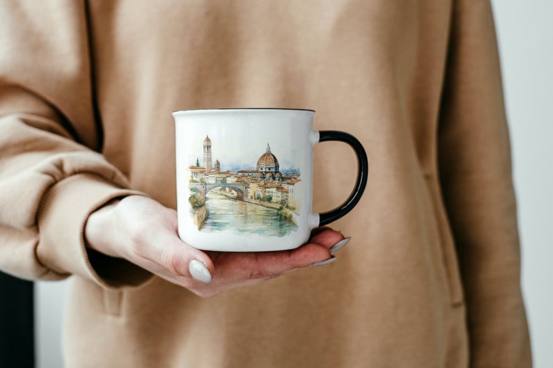 K&ouml;nnte beinhalten: Wei&szlig;e Keramiktasse mit schwarzem Henkel. Die Tasse zeigt eine Aquarell-Illustration einer Stadtlandschaft mit einer Br&uuml;cke und einem kuppelf&ouml;rmigen Geb&auml;ude.