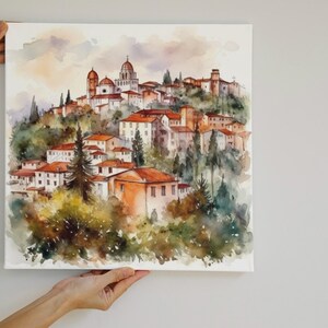 K&ouml;nnte beinhalten: Aquarellgem&auml;lde einer kleinen Stadt, die sich an einen H&uuml;gel schmiegt. Die Geb&auml;ude sind in Orange-, Rot- und Braunt&ouml;nen gemalt, umgeben von gr&uuml;nen B&auml;umen. Der Himmel ist in einem sanften Blau mit rosa und violetten Farbt&ouml;nen gehalten.