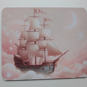 May include: A pink and white mousepad with a ship sailing through clouds. The ship has white sails and a skull and crossbones flag. The text "To Wonderland..." is written on the mousepad.