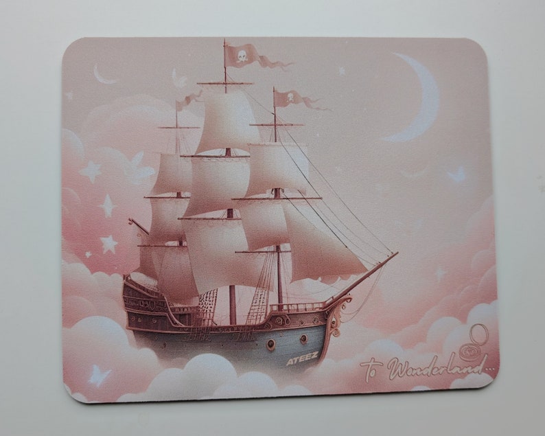 May include: A pink and white mousepad with a ship sailing through clouds. The ship has white sails and a skull and crossbones flag. The text "To Wonderland..." is written on the mousepad.