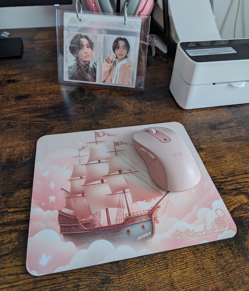 May include: Pink mousepad with a pink mouse on top. The mousepad features a pink and white illustration of a ship sailing on clouds with the text "To Wonderland..." and "ATEEZ" on it.