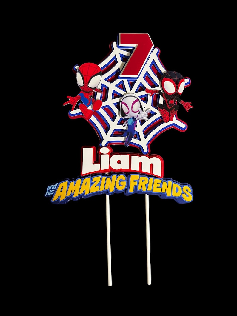 May include: A red, white and blue cake topper with a spiderweb design. Three Spiderman characters are on the web, and the number 7 is in the centre. The text "Liam and his AMAZING FRIENDS" is below the web.