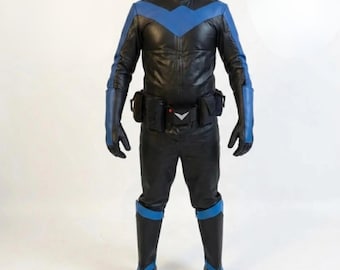 May include: Black and blue superhero costume. The costume includes a black leather-like jacket with blue accents on the shoulders and chest, matching pants, gloves, and boots. A utility belt with pouches and a white emblem complete the outfit.