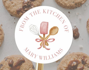 Puede incluir: Pegatina redonda blanca con el texto "From the Kitchen of Mary Williams" en letras rosas. Una espátula rosa, una cuchara de madera y un batidor de alambre se cruzan en el centro de la pegatina.