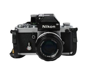 May include: A vintage Nikon camera with a black body and silver accents. The lens is black with the text "Nikon" and other details. The camera has a leather strap and the Nikon logo is visible on the top.