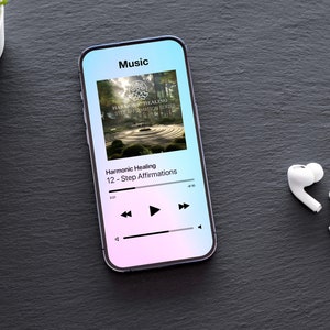 Puede incluir: Un teléfono inteligente muestra una interfaz de aplicación de música con el texto «Música» en la parte superior. La pantalla muestra la carátula de un álbum y el título «Harmonic Healing 12-Step Affirmations». Auriculares inalámbricos blancos junto al teléfono. Una pequeña planta en el fondo.