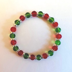 May include: A circular beaded bracelet featuring alternating translucent red and green faceted glass beads. Each bead is separated by a small, silver-toned metal spacer ring that contains tiny clear embedded crystals, creating a repeating pattern.