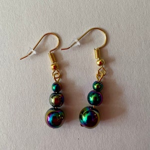 May include: A pair of gold earrings with three iridescent black beads on each earring.