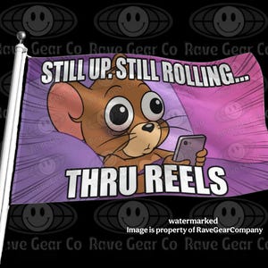 May include: A rectangular flag featuring a cartoon brown mouse with large eyes holding a smartphone. The background is a purple radial pattern. The text reads STILL UP. STILL ROLLING... THRU REELS in bold white letters with a black outline.
