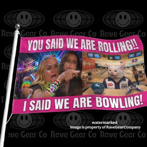 May include: A rectangular flag featuring a pink border with the text YOU SAID WE ARE ROLLING!! and I SAID WE ARE BOWLING!. The center displays a split image of a person with colorful bracelets pointing and a white cat in a bowling shirt at a lane.