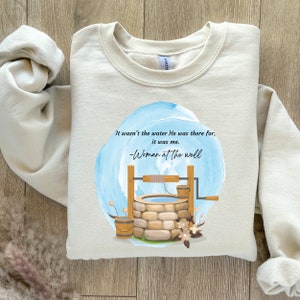 May include: A beige sweatshirt with a blue watercolor design of a well with a bucket and a quote that reads "It wasn't the water He was there for, it was me. -Woman at the well"