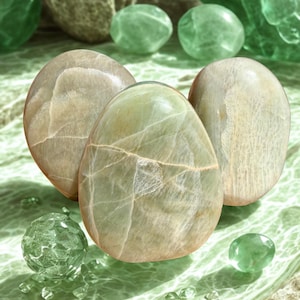 May include: An assortment of polished stones in shades of green and tan. Three large, oval-shaped stones are the focal point, with smaller, spherical and pebble-like stones scattered around. The stones have a smooth, reflective surface, suggesting they are gemstones or decorative objects.