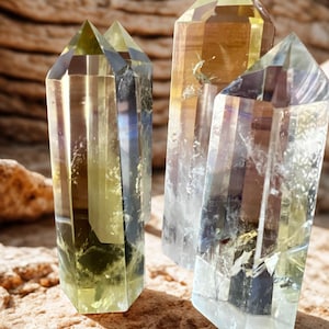May include: Four clear quartz crystal points with yellow and brown hues. The crystals are faceted and stand upright on a textured, light brown surface. The crystals have a natural, earthy appearance.