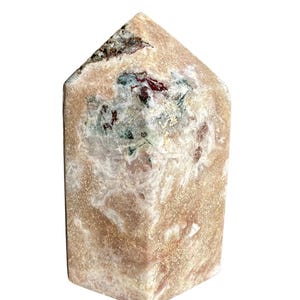 May include: A polished, rectangular crystal tower with a flat top. The stone features a mix of colors, including peach, white, green, and red. The crystal has a textured surface and is set against a white background.