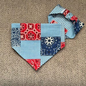 May include: A triangular pet bandana featuring a patchwork design of red, navy blue, and light blue fabric squares. The patterns include floral paisley motifs, small gingham checks, and solid light blue squares. It includes a matching scrunchie.