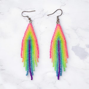 May include: A pair of vibrant, beaded earrings in a rainbow color scheme. The earrings feature a fringe design with a gradient of pink, yellow, green, blue, and purple beads. The earrings have silver-tone ear wires.