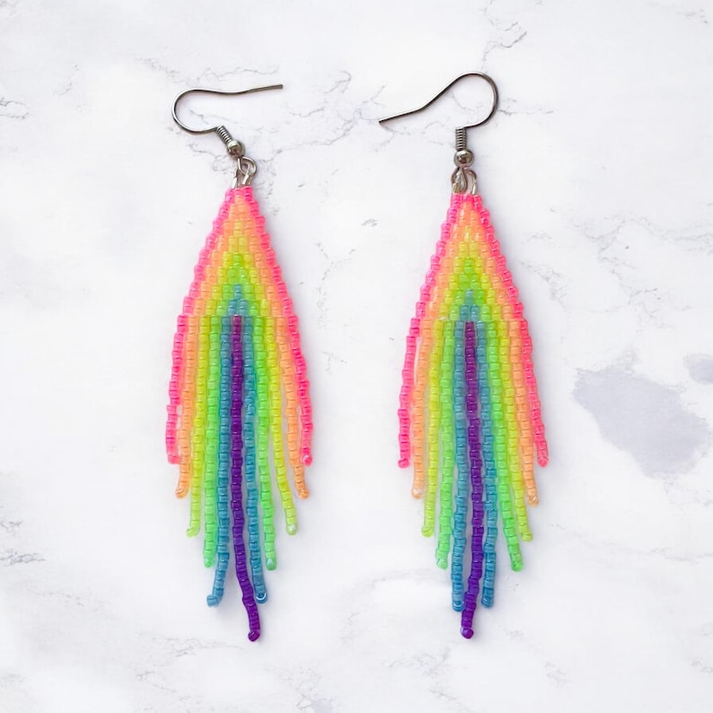 May include: A pair of vibrant, beaded earrings in a rainbow color scheme. The earrings feature a fringe design with a gradient of pink, yellow, green, blue, and purple beads. The earrings have silver-tone ear wires.