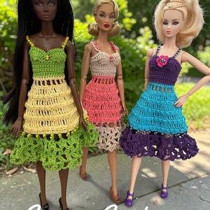 May include: Three fashion dolls wearing handmade crochet sundresses in shades of green, yellow, pink, beige, blue, and purple. The dresses have intricate openwork designs. The text "Summer Sundresses" is at the bottom of the image.