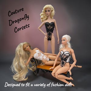 May include: Three fashion dolls wearing intricate lace corsets in black and white. One doll stands while two others sit on a small bench. The text reads: Couture Dragonfly Corsets. Designed to fit a variety of fashion dolls.