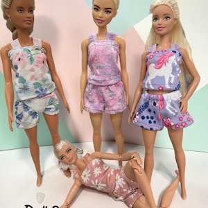 Könnte beinhalten: Vier Puppen tragen Puppenpyjamas. Die Pyjamas umfassen Tanktops und Shorts in verschiedenen Blumen- und Mustermotiven. Der Text "Doll Pajamas" ist unten im Bild in Schwarz gedruckt.