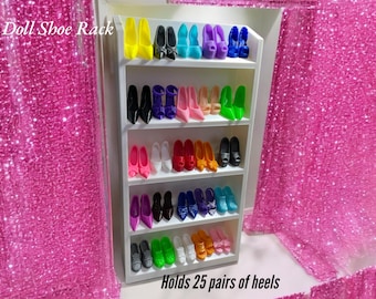 Puede incluir: Un estante blanco de cinco niveles para zapatos de muñeca que exhibe 25 pares de tacones altos en miniatura de varios colores, incluyendo amarillo, negro, azul, rosa, rojo, naranja, verde y blanco. El texto Doll Shoe Rack y Holds 25 pairs of heels es visible.