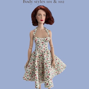 Könnte beinhalten: Eine Puppe in einem Kleid mit Blumenmuster und weißen Schuhen. Das Kleid hat einen Neckholder-Ausschnitt und einen weiten Rock mit einem Muster aus roten und rosa Blumen und grünen Blättern auf cremefarbenem Hintergrund. Der Text "SHOES FOR RT DOLLS" steht oben.