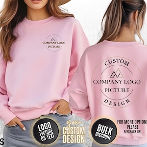May include: Pink sweatshirt with a custom design option. The design features a circle with the text "CUSTOM DESIGN" and a triangle logo with the text "COMPANY LOGO PICTURE".