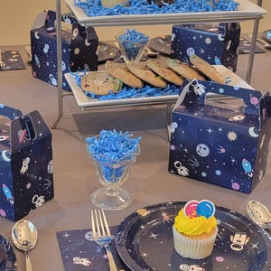 Juego de decoraciones para fiestas del espacio exterior: 36 platos, servilletas y cajas de recuerdos con temática de astronauta y cohete para cumpleaños infantiles.