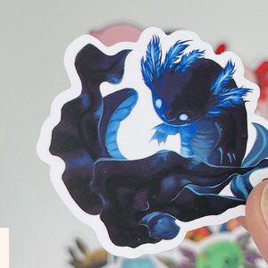 Op de afbeelding: Een sticker met een zwarte en blauwe axolotl met blauwe gevederde kieuwen. De axolotl zwemt in een donkerblauwe werveling.